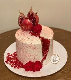 a white cake with pomegranates on top sitting on a wooden table