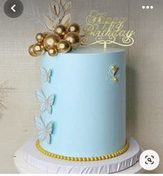 a blue and gold birthday cake with butterflies on it's top, sitting on a white pedestal