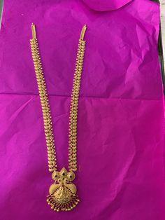 a gold necklace is displayed on a purple paper with a pink bag in the background