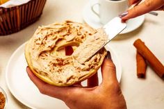 a person holding a knife over a doughnut on a plate with cinnamon sticks around it