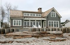 a gray house with white windows and wood logs on the ground in front of it