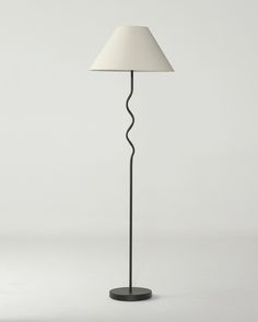 a floor lamp with a white shade on the base and a black metal pole in front of it