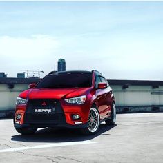 a red car is parked in an empty parking lot next to a building and sky