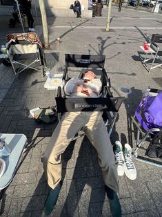 a man sitting in a stroller on the street with his feet up and head down