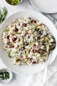 a white bowl filled with chicken salad next to other bowls and spoons on a marble table