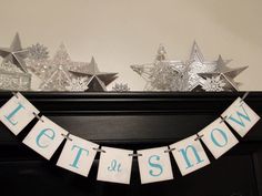 a banner that says let it snow hanging from a mantle with silver stars on top