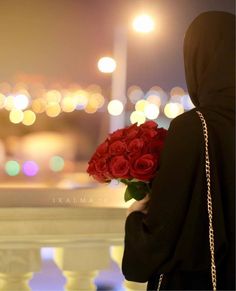 a woman holding a bouquet of red roses in her hand and looking at the city lights