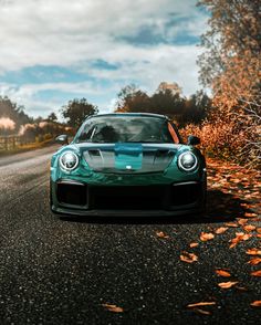 a green sports car parked on the side of a road in front of some trees