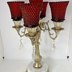 four red glass candlesticks sitting on top of a white base with crystal beads