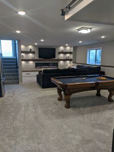 a pool table in the middle of a living room with stairs leading up to it