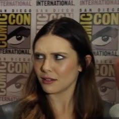 a woman with long brown hair and blue eyes is talking to someone in front of a comic panel