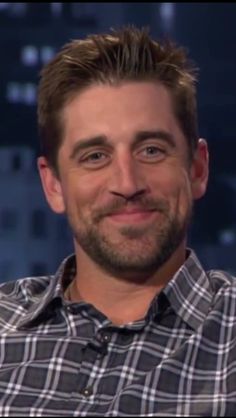 a man with a goatee smiles at the camera while sitting in front of a window