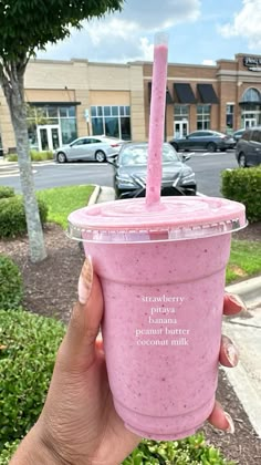 a person holding up a pink smoothie in front of a building