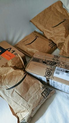 some brown paper bags sitting on top of a white sheet covered bed next to each other