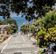 an empty street with cars parked on the side and trees lining the road in front of it