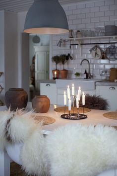 a dining room table with white chairs and candles in the center surrounded by fur pillows