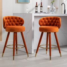 two orange velvet bar stools in front of a counter with bottles and glasses on it