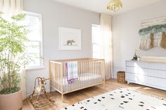 a baby's room with a crib, dresser, and potted plant