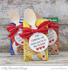 two wooden spoons with labels on them sitting in front of some cereal bags and boxes