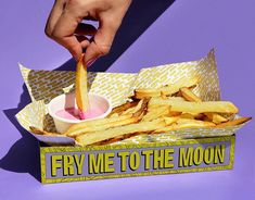 a hand is dipping french fries into a box that says fry me to the moon