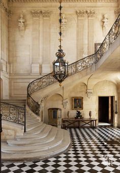 an ornate staircase with black and white checkered flooring, chandelier and table