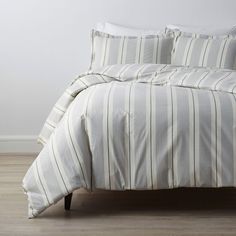 a bed with white and grey striped comforter on top of wooden floor next to wall