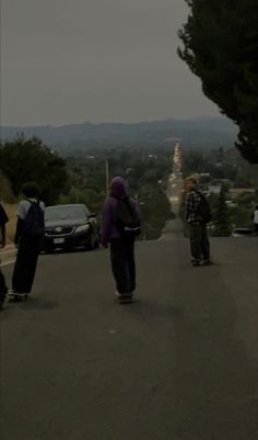 three skateboarders are riding down the street in front of some cars and trees