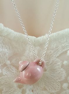 a pink pig necklace on a white lace surface with a silver chain hanging from it's back