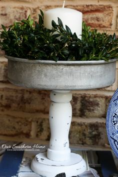 a candle is sitting on top of a cake plate with greenery in the middle