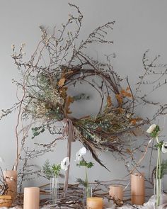 a table topped with lots of vases filled with flowers and greenery next to candles