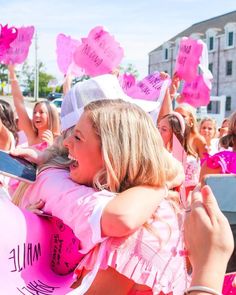 two girls hugging each other in front of a group of people holding up pink signs