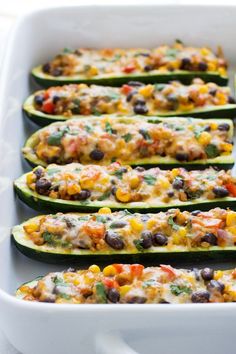 stuffed zucchini boats filled with black beans, cheese and other toppings in a white baking dish