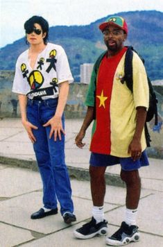 two young men standing next to each other on top of a stone walkway with mountains in the background