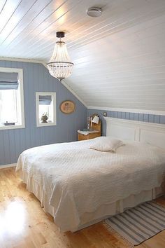 a white bed sitting in a bedroom next to a window and a rug on top of a hard wood floor