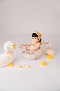 a baby sitting in a bathtub surrounded by rubber ducks and rubber ducklings on a white background