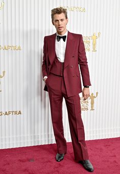 a man in a red suit and bow tie posing for the camera on a red carpet