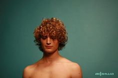 a man with curly hair standing in front of a blue background