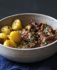 a bowl filled with meat and potatoes on top of a blue cloth next to a fork