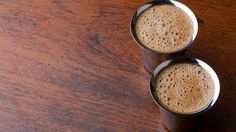 two cups of coffee sitting on top of a wooden table next to eachother