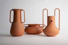 three clay vases sitting next to each other on a white surface with two handles