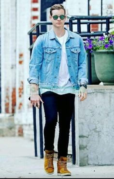 a young man wearing sunglasses and a jean jacket is walking down the street with his hands in his pockets