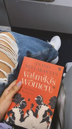 a person sitting down reading a book with ripped jeans on their lap and holding the book