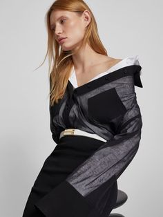 a woman sitting on top of a stool wearing a black and white shirt with an off the shoulder design