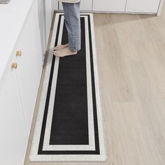 a person standing on a black and white rug in the middle of a kitchen area