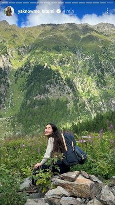 a woman sitting on top of a rock next to a lush green forest covered hillside