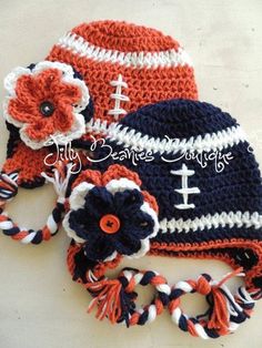 two crocheted hats with flowers are laying on the table together, one has an orange and white flower