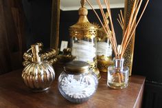 a wooden table topped with two vases filled with white flowers and reeds next to a mirror