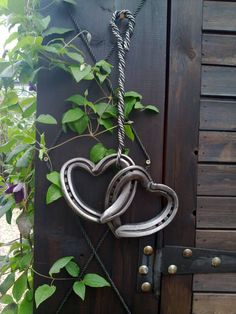 a couple of metal hearts hanging from a wooden fence next to a planter with green leaves on it