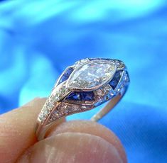 a close up of a person's hand holding a diamond and sapphire ring