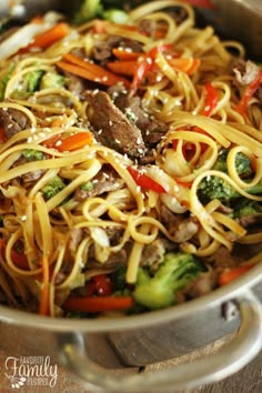 a skillet filled with beef noodles and broccoli, carrots and peppers